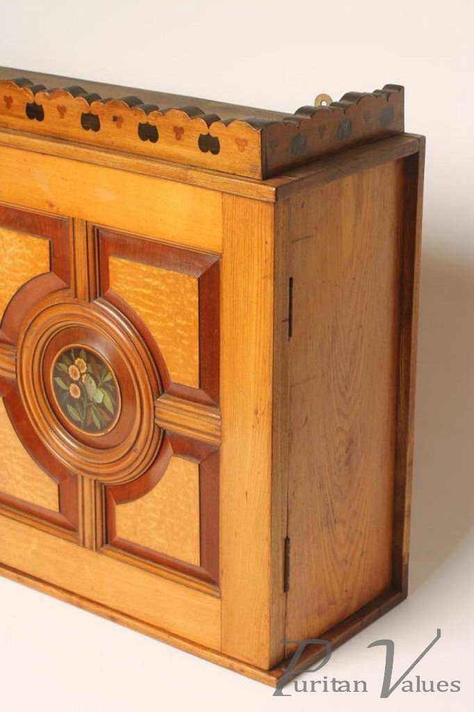AN_AESTHETIC_ASH_WALL_CABINET_gallery_inlaid_with_alternating_trefoil_and_shield_motifs_two_doors_each_with_burr_ash_fielded_quarter_panels_centred_by_a_painted_floral_roundel_43_75_x_10_75_x_25__master